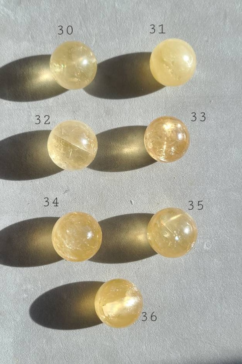May include: Six yellow citrine crystal spheres, numbered 30 to 36, arranged in rows on a grey surface.