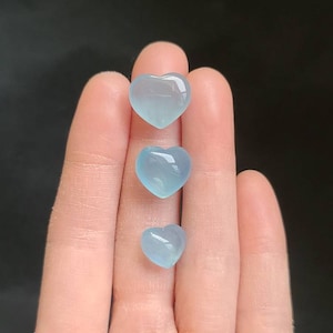 May include: Three heart-shaped stones in different sizes, all a pale blue colour. The stones are arranged vertically, with the largest at the top and the smallest at the bottom.