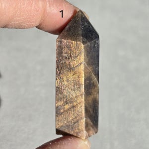 Könnte beinhalten: Eine goldene Labradorit-Kristallspitze mit einer dunkelgrauen Basis und irisierendem Schimmer. Der Kristall ist etwa 5 cm lang.