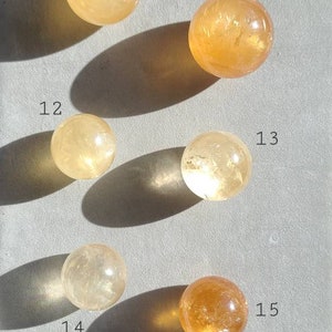 May include: Five yellow and orange crystal spheres, numbered 10 through 15, on a grey surface. The spheres are various shades of yellow and orange, with some having a more translucent appearance.