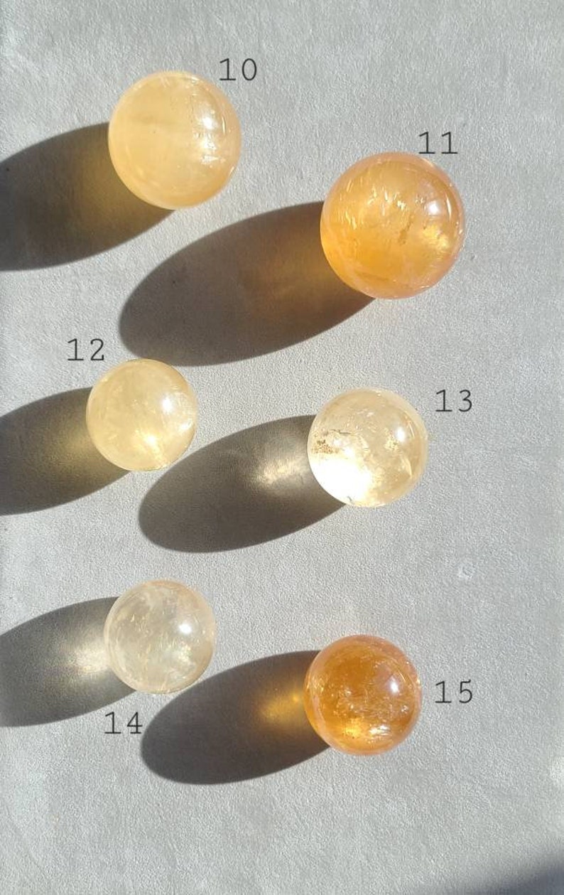 May include: Five yellow and orange crystal spheres, numbered 10 through 15, on a grey surface. The spheres are various shades of yellow and orange, with some having a more translucent appearance.