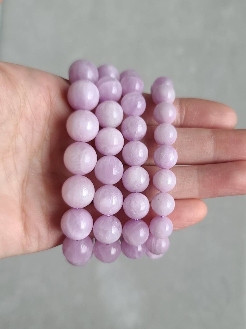 Peut inclure: Quatre rangs de perles de pierres pr&eacute;cieuses de couleur lavande, chaque rang est un bracelet avec des perles rondes, les bracelets sont empil&eacute;s les uns sur les autres sur une main.