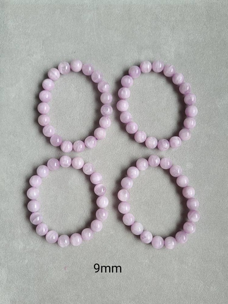 Peut inclure: Quatre bracelets de couleur lavande faits de perles rondes, chaque bracelet mesure 9 mm de diam&egrave;tre. Les bracelets sont dispos&eacute;s en carr&eacute; sur une surface grise.