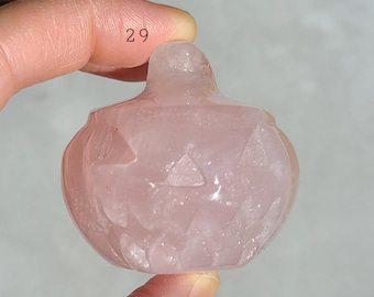 May include: A pink rose quartz pumpkin carving. The carving has a detailed face with a triangular nose and eyes.