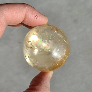 May include: A golden citrine sphere with iridescent rainbow flashes. The sphere is approximately 5 cm in diameter.