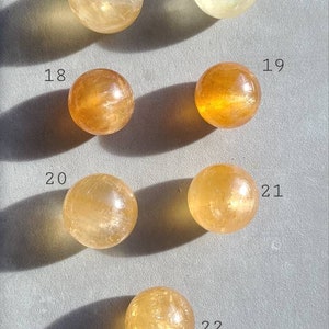 May include: Seven smooth, round, polished citrine spheres of varying sizes, numbered 16 through 22. The spheres are arranged in rows on a light grey surface.