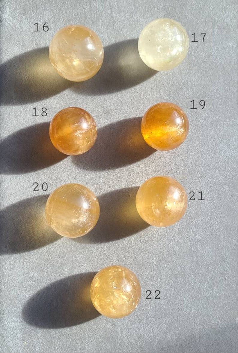 May include: Seven smooth, round, polished citrine spheres of varying sizes, numbered 16 through 22. The spheres are arranged in rows on a light grey surface.