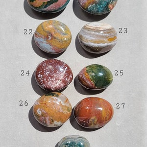 Pu&ograve; includere: Una collezione di otto pietre levigate di forma ovale con vari motivi e colori, tra cui rosso, verde, marrone, bianco e giallo. Le pietre sono numerate da 20 a 28.