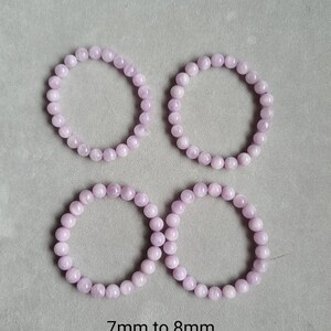 Peut inclure: Quatre bracelets en perles de couleur lilas clair, chacun d'un diam&egrave;tre de 7 &agrave; 8 mm. Les bracelets sont dispos&eacute;s en carr&eacute; sur une surface grise.