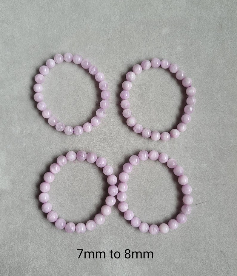Peut inclure: Quatre bracelets en perles de couleur lilas clair, chacun d'un diam&egrave;tre de 7 &agrave; 8 mm. Les bracelets sont dispos&eacute;s en carr&eacute; sur une surface grise.