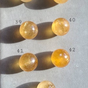 May include: Ten round, smooth, polished, yellow citrine spheres, numbered 37 through 43. The spheres are arranged in two rows of five, with the numbers written next to each sphere.