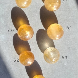 May include: Seven polished, golden yellow, crystal spheres, numbered 58 through 64, arranged in a grid pattern on a grey surface.