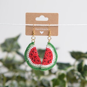 Puede incluir: Pendientes de rodaja de sandía de ganchillo con ganchos dorados. Los pendientes cuelgan de una tarjeta marrón con la palabra "Handmade" escrita en ella.