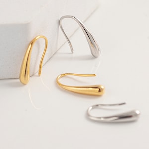 May include: Three pairs of minimalist earrings in gold and silver. The earrings are teardrop shaped and have a simple, elegant design.
