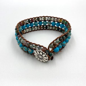 May include: A multi-strand bracelet with brown leather cord and turquoise and green gemstone beads. The bracelet has a silver flower clasp.