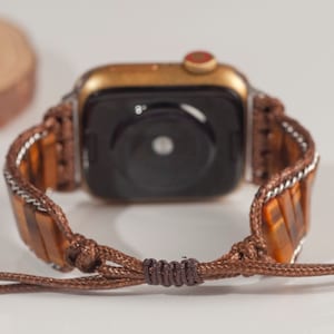 May include: A brown leather watch band with a gold Apple Watch. The band is made of braided leather with a tiger's eye stone accent.