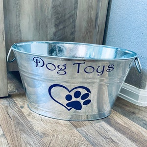 May include: A silver metal dog toy bin with the words "Dog Toys" and a blue paw print inside a heart on the side.