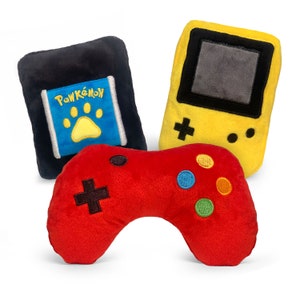 May include: Three plush toys shaped like a video game controller, a handheld game console, and a game cartridge. The game cartridge is blue and yellow with the text "PawKémon" on it. The game console is yellow with a black screen and buttons. The controller is red with black buttons.