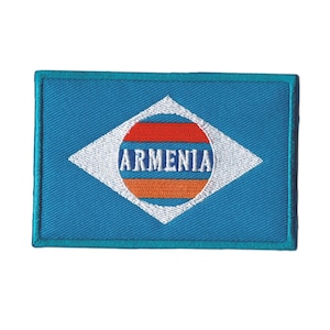 May include: A rectangular embroidered patch featuring a blue background with a white diamond shape in the center. Inside the diamond is a circular emblem with horizontal red, blue, and orange stripes and the white text ARMENIA across the middle.