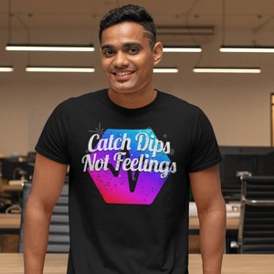 Op de afbeelding: Een zwart T-shirt met een kleurrijk grafisch ontwerp met de tekst "Catch Dips Not Feelings".
