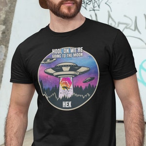 May include: A black t-shirt with a graphic of a UFO and the text "Hold on we're going to the moon" and "Hex" in a circle.