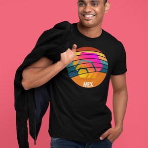 May include: A black t-shirt featuring a retro-style graphic of a hexagon with the word "HEX" underneath. The graphic is in shades of orange, yellow, pink, blue, and green.