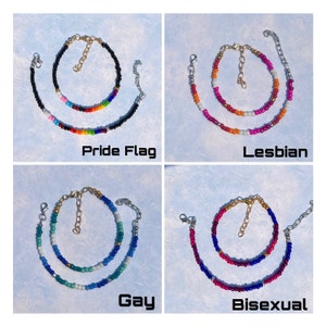 K&ouml;nnte beinhalten: Vier Armb&auml;nder mit Perlen und verstellbaren Ketten. Jedes Armband hat ein anderes Farbschema: Pride Flag, Lesbian, Gay und Bisexual. Die Armb&auml;nder werden auf einem hellblauen Hintergrund pr&auml;sentiert.