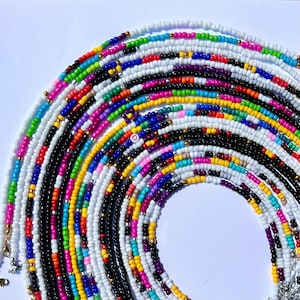 May include: A colorful beaded necklace with multiple strands of different colors, including white, black, pink, blue, and yellow. The necklace is arranged in a semi-circle shape, with the ends of the strands hanging down.