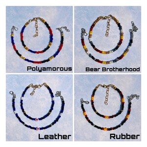 K&ouml;nnte beinhalten: Vier Armb&auml;nder mit Perlen und verschiedenen Farbmustern sowie den Texten: "Polyamorous", "Bear Brotherhood", "Leather" und "Rubber". Jedes Armband hat eine goldfarbene Kette und einen Verschluss.