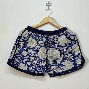 Könnte beinhalten: Blau-weiß gemusterte Shorts mit marineblauen Zierleisten. Die Shorts hängen an einem Holzbügel vor einer weißen Wand. Die Shorts haben einen Kordelzug in der Taille und Taschen.