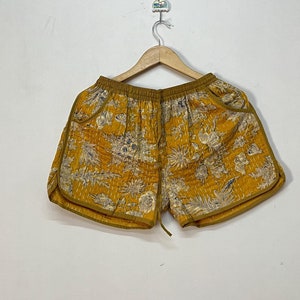 Könnte beinhalten: Gelbe gesteppte Shorts mit Blumenmuster. Die Shorts haben einen Kordelzugbund und einen gelben Saum.