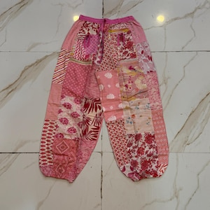 Puede incluir: Pantalones rosas de patchwork con cintura con cordón. Los pantalones presentan varios parches de tela estampada floral en tonos rosas y rojos. Los pantalones están hechos de un material ligero.