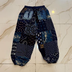 May include: Blue patchwork trousers with a drawstring waist. The trousers feature a variety of blue patterns, including floral, geometric, and abstract designs. The trousers are made of a lightweight fabric and have a relaxed fit.