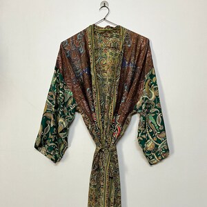 May include: A long, open-front robe with a paisley pattern in shades of green, brown, and gold. The robe has long sleeves and a matching tie belt. The garment is hanging on a metal hanger against a white background.