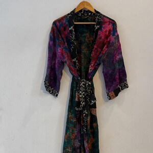 May include: A long-sleeved, floor-length robe featuring a vibrant, multi-colored tie-dye pattern in shades of purple, pink, and deep green. The garment includes a black collar and a matching tie-waist belt, both decorated with a white geometric print.