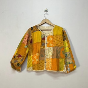 Może przedstawiać: Kurtka patchwork w odcieniach żółtego, pomarańczowego i brązowego, z pikowanym wzorem. Kurtka posiada okrągły dekolt, długie rękawy i zapięcia na guziki. Tkanina to mieszanka wzorzystych i gładkich elementów.