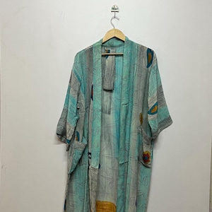 May include: A long, open-front kimono robe in shades of teal, gray, and yellow, adorned with a leaf and floral pattern. The robe is hanging on a wooden hanger, showcasing its flowing design and lightweight fabric.
