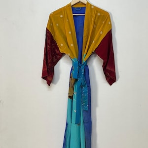 Könnte beinhalten: Ein farbenfroher Patchwork-Kimono mit lebendigem Design. Der Kimono hat eine senfgelbe Oberseite, ein blaues Innenfutter und rote Ärmel. Der untere Teil wechselt von Türkis zu Blau. Ein passender blauer Schärpengürtel bindet die Taille.