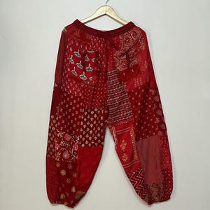 May include: Red patchwork pants with a drawstring waist and elastic cuffs. The pants are made of a variety of fabrics with different patterns, including floral, geometric, and paisley.