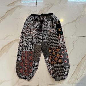 以下が含まれることがあります： 黒いドローストリングウエストのパッチワークパンツ。パンツは、黒、白、茶色、赤、オレンジ色のさまざまな模様の生地パッチが特徴です。デザインには、花柄、幾何学模様、ストライプ模様が含まれています。