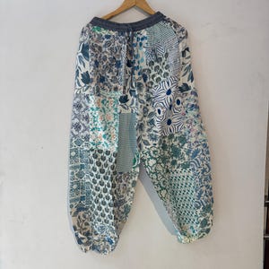 Peut inclure: Pantalon ample à motif patchwork composé de divers imprimés floraux, géométriques et cachemire dans des tons bleu, vert et blanc. Le pantalon possède une taille élastique gris foncé avec un cordon de serrage et des chevilles élastiquées.