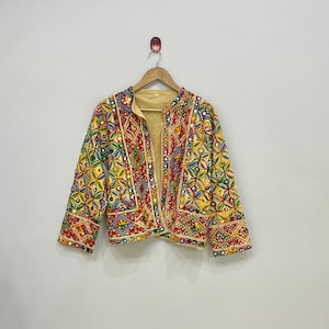 Puede incluir: Una chaqueta bordada en amarillo, rojo y azul con adornos de espejo. La chaqueta tiene un cuello mandarín y mangas largas.