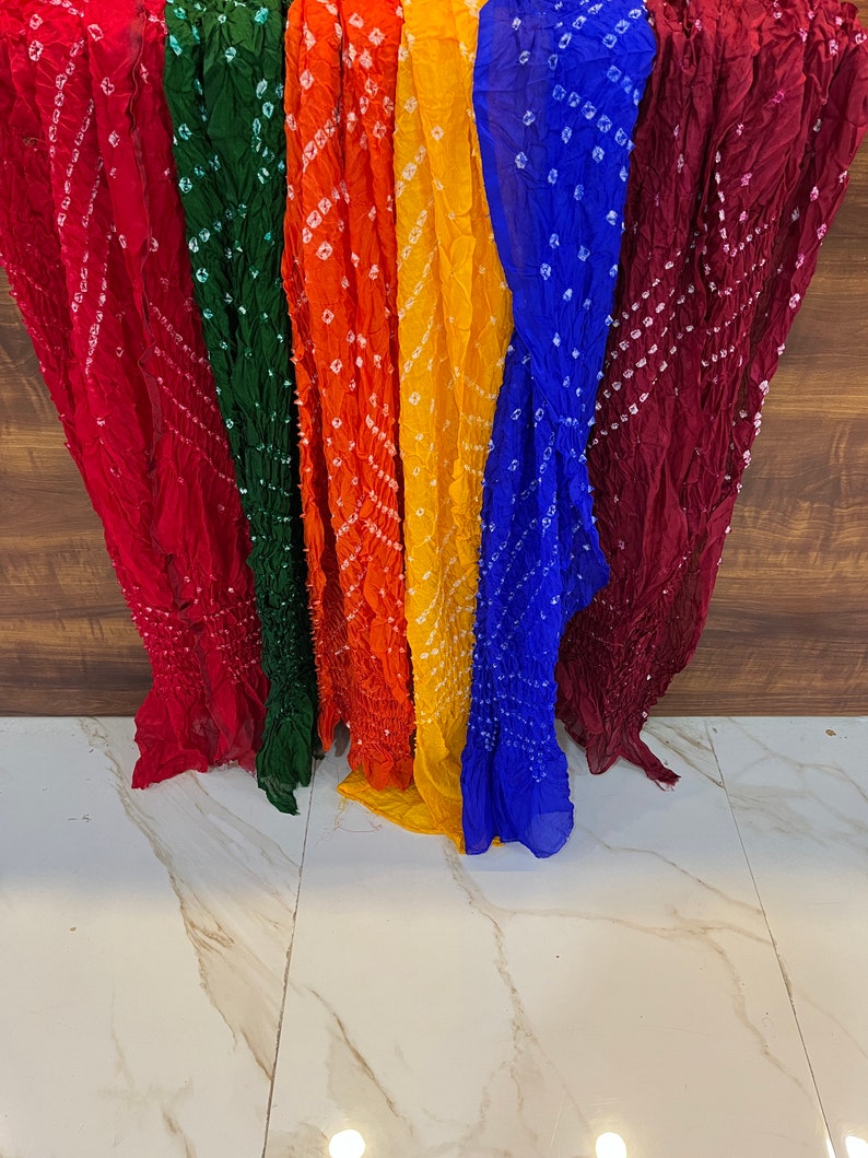 Peut inclure: Une collection de six foulards color&eacute;s avec un motif tie-dye et des points blancs. Les foulards sont dispos&eacute;s en rang&eacute;e, avec le foulard rouge &agrave; gauche et le foulard marron &agrave; droite. Les foulards sont faits d'un tissu doux et l&eacute;ger.