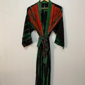 May include: A long, black robe with a tie-waist, hanging on a wooden hanger. The robe features a vibrant design with orange and green accents across the shoulders and down the front. Green vertical stripes run down the length of the robe.