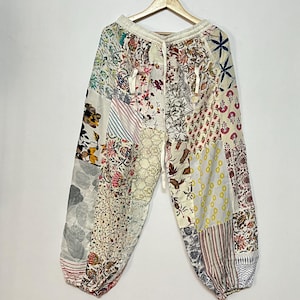 Op de afbeelding: Witte katoenen broek met een patchwork-ontwerp met verschillende bloemen- en geometrische patronen. De broek heeft een elastische tailleband en een trekkoord.