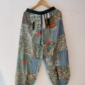 Peut inclure: Pantalon ample présentant un motif patchwork avec divers imprimés floraux et géométriques dans des tons de vert sauge, bleu et blanc. Le pantalon possède une taille élastique avec un cordon de serrage et des chevilles élastiquées.