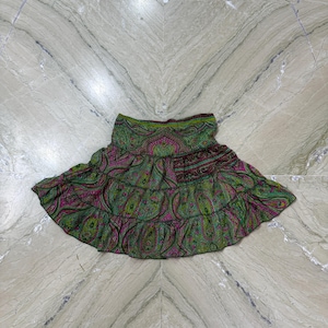 Könnte beinhalten: Ein gestufter Minirock mit einem lebendigen Paisley-Muster in Grün-, Magenta- und Schwarztönen. Der Rock verfügt über einen breiten, elastischen Bund und eine ausgestellte Silhouette mit zwei horizontalen Rüschen für einen vollen Look.