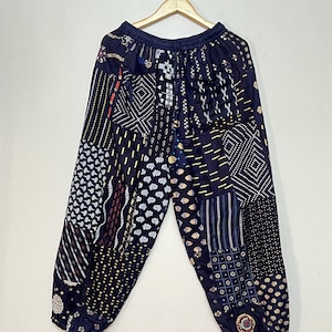 Peut inclure: Pantalon noir avec un motif patchwork présentant divers motifs géométriques et floraux en blanc, or et rouge.