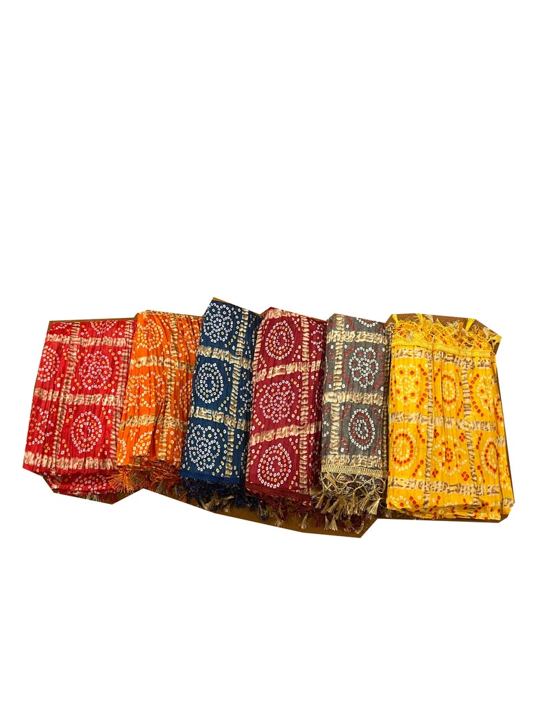 May include: Five folded fabric squares with a patterned design. The squares are in shades of red, orange, blue, burgundy, and yellow. Each square has a gold trim and a fringe.