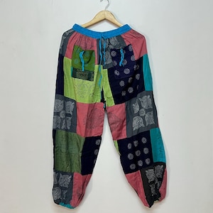May include: Patchwork pants featuring a vibrant mix of rectangular fabric panels in shades of pink, navy blue, lime green, and teal. The garment includes an elastic waistband with a bright blue drawstring, two front pockets, and elastic cuffs.